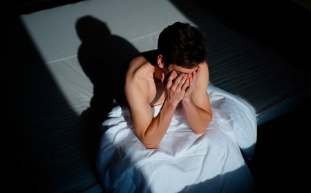 Мужчина сидит на кровати склонив голову