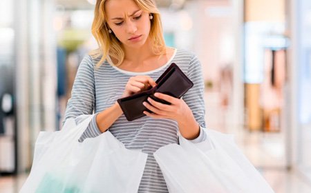 Девушка с пакетами огорчённо смотрит в пустой кошелёк