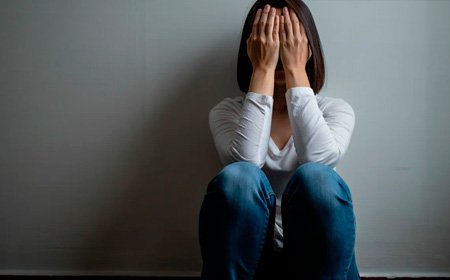 Женщина сидит на полу, закрыв лицо руками